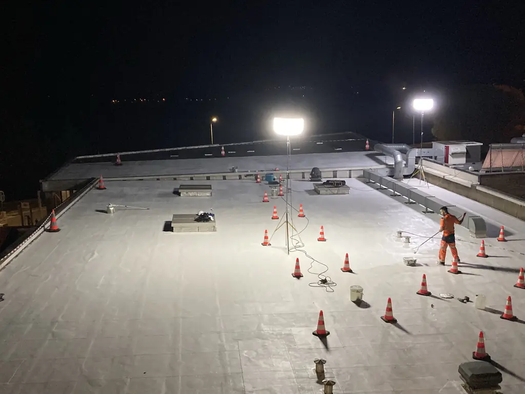 Chantier de toiture de nuit, éclairé par des projecteurs et balisé de cônes