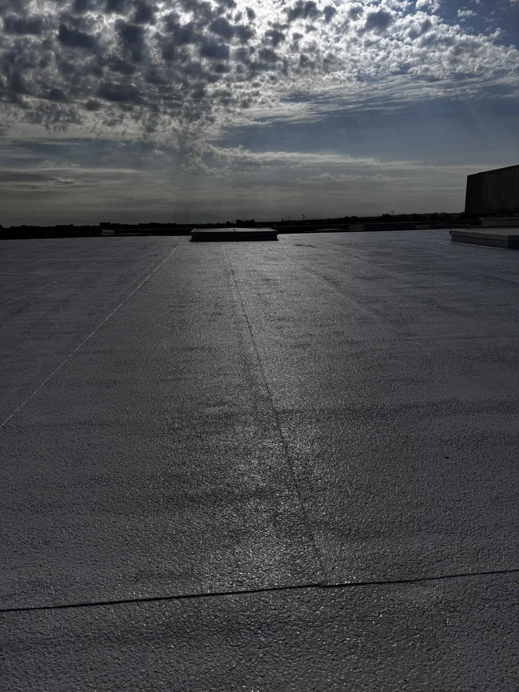 Grande toiture-terrasse en membrane d’étanchéité, à contre-jour sous un ciel nuageux